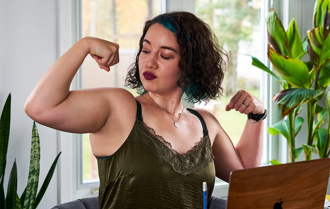 CSD_About Me_Header Chelsey devant son ordinateur portable en train de fléchir ses biceps.